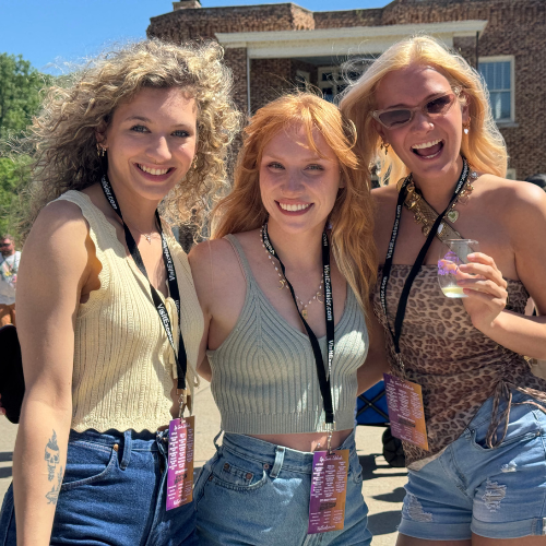 Three women smiling and holding wine samples at a sunny outdoor wine festival in Missouri