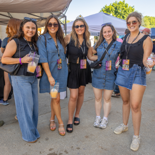 Group of women wearing event badges holding drinks and smiling at a wine festival in Downtown Excelsior Springs