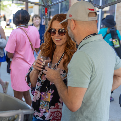 Man and woman tasting wine and chatting at a vendor booth during a downtown wine festival