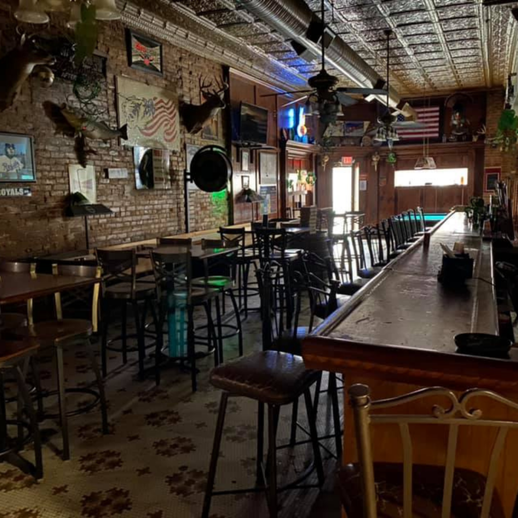 Interior of Atlas Saloon Brewery with exposed brick walls, mounted decor, high-top tables, and a long bar in a historic downtown setting.
