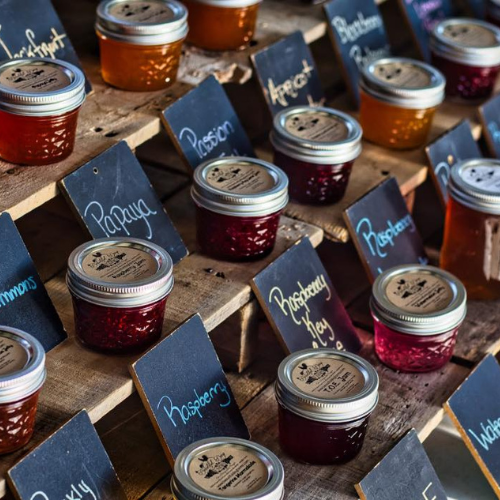 Assorted jars of homemade jams from Beautiful Day Farms labeled by flavor on a rustic display table