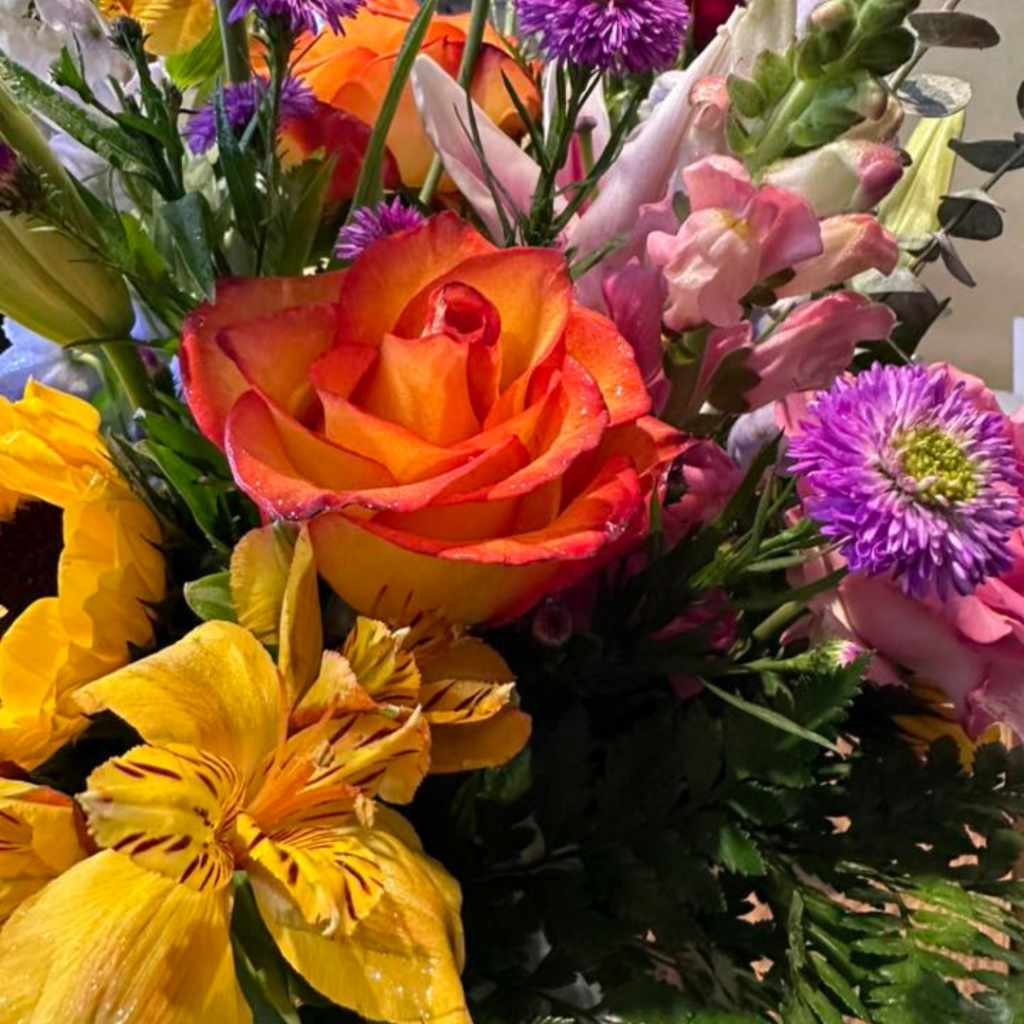 Colorful bouquet featuring orange roses, yellow lilies, and purple flowers arranged in a fresh floral display.