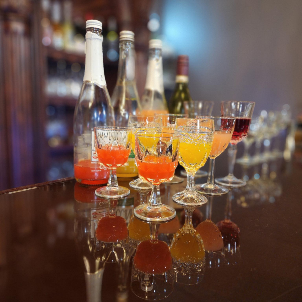 Assorted sparkling wine and mimosa-style drinks in decorative glasses on a bar at Casa Di Vite wine bar.