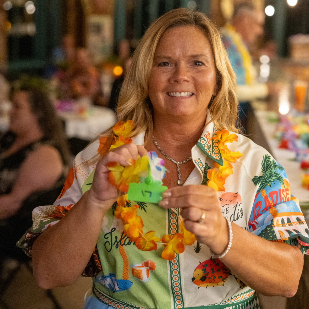 Annual Dinner attendee Jill smiles while holding her winning diamond fundraiser ticket during the 2025 luau celebration.