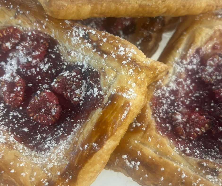 Close-up of flaky fruit pastries filled with strawberries and dusted with powdered sugar.
