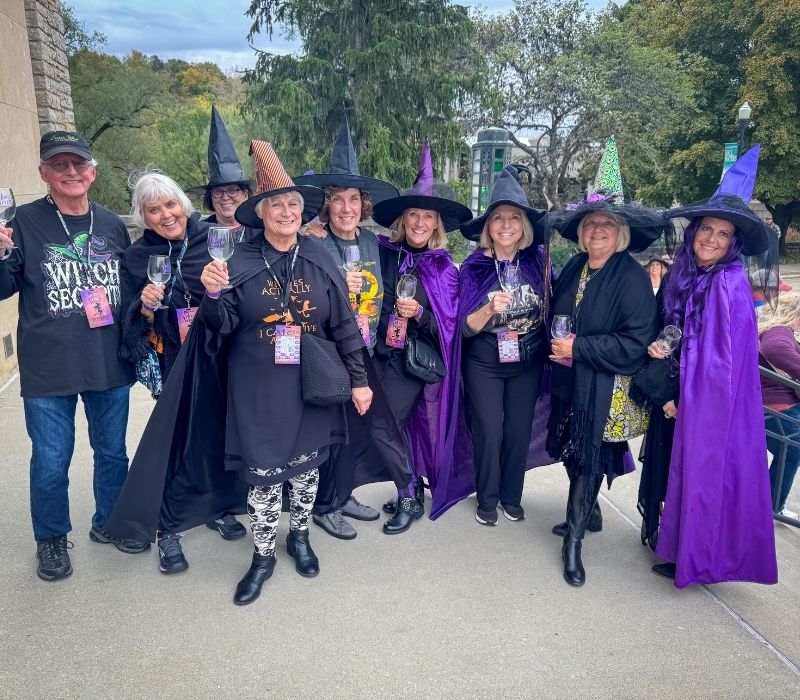 Friends dressed as witches pose with tasting glasses during Witch Way to the Wine.