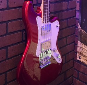 Red electric guitar mounted on a brick wall under stage lighting, representing live music entertainment.