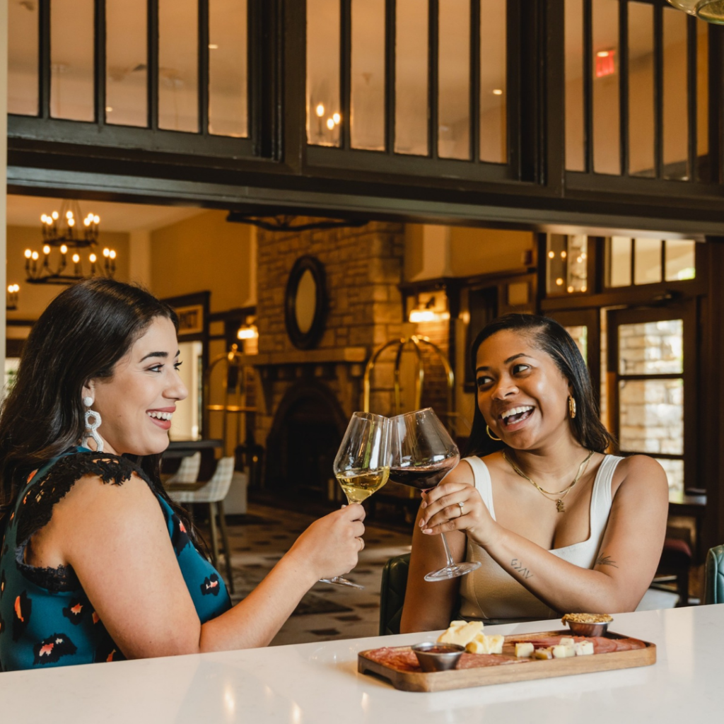 Two guests enjoy wine and a charcuterie board inside The Elms Hotel & Spa in Excelsior Springs, Missouri, highlighting the hotel's dining and social experience.