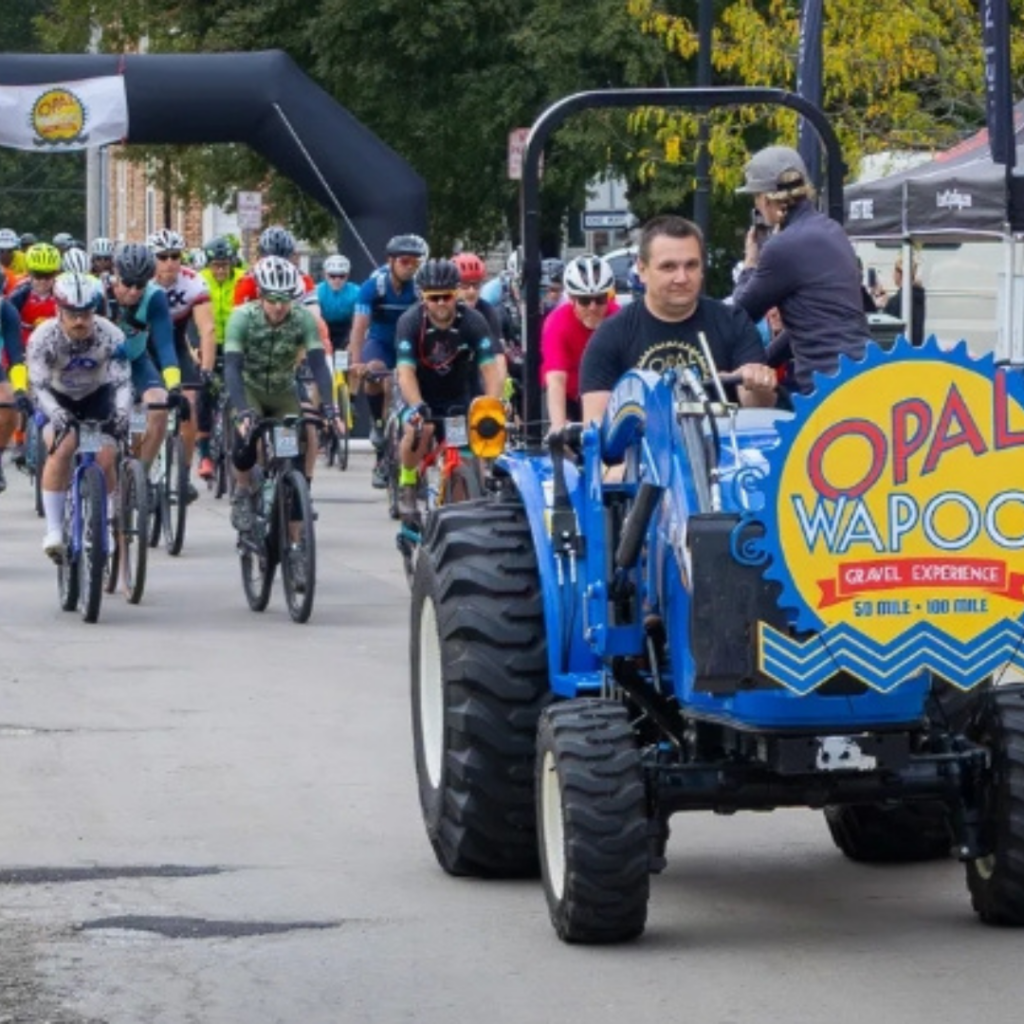 Participants begin the Opal Wapoo Gravel Experience as cyclists ride through Downtown Excelsior Springs following the event's lead vehicle and start arch.
