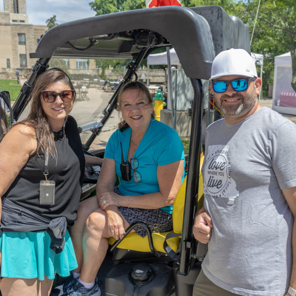 Carol Baxter sits in a utility vehicle with event volunteers during a festival, helping coordinate event operations in Downtown Excelsior Springs.