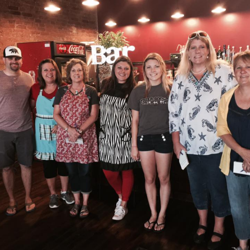 Carol Baxter stands with Downtown Excelsior Partnership volunteers and community members during a downtown event, showcasing years of volunteer service and community involvement.