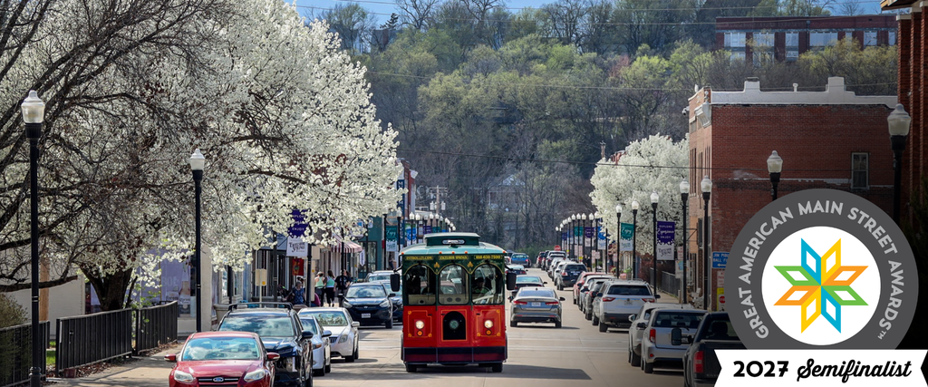 Excelsior Springs trolley travels down a downtown street lined with blooming trees and historic storefronts.