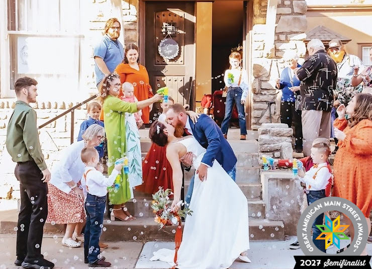 A newly married couple kisses outside a downtown building as family and friends blow bubbles.